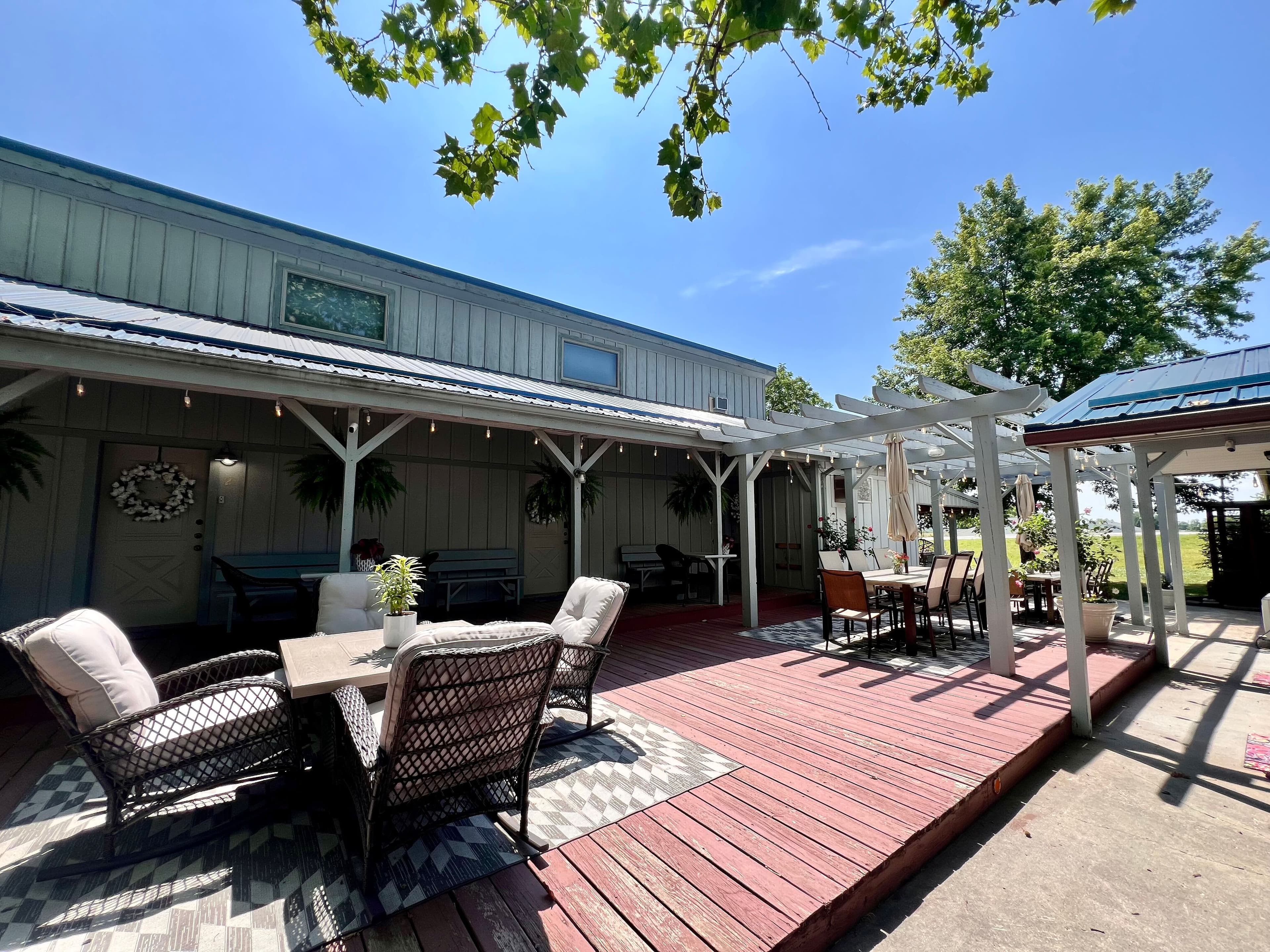 Outdoor dining area on a raised patio with an area rug, potted plants, and a pergola