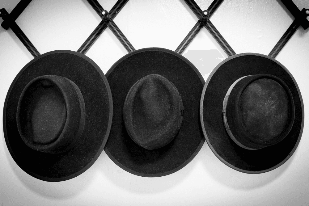 Three black amish hats hanging on black wall hat rack