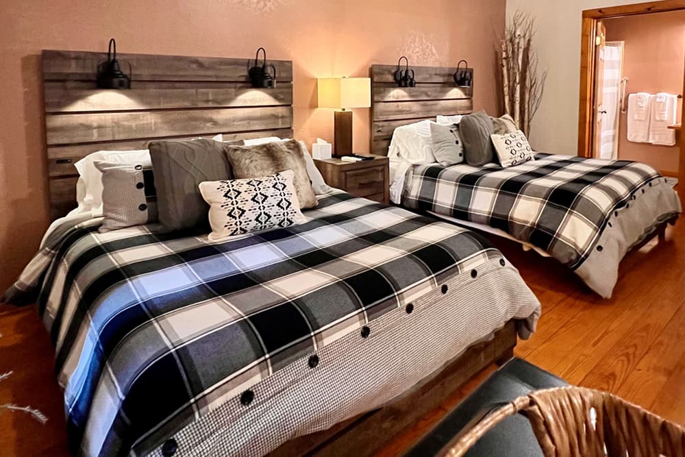 Pine log bed, plaid coverlet, green walls, pine floors, chest at foot of bed and pine nightstand with lamp