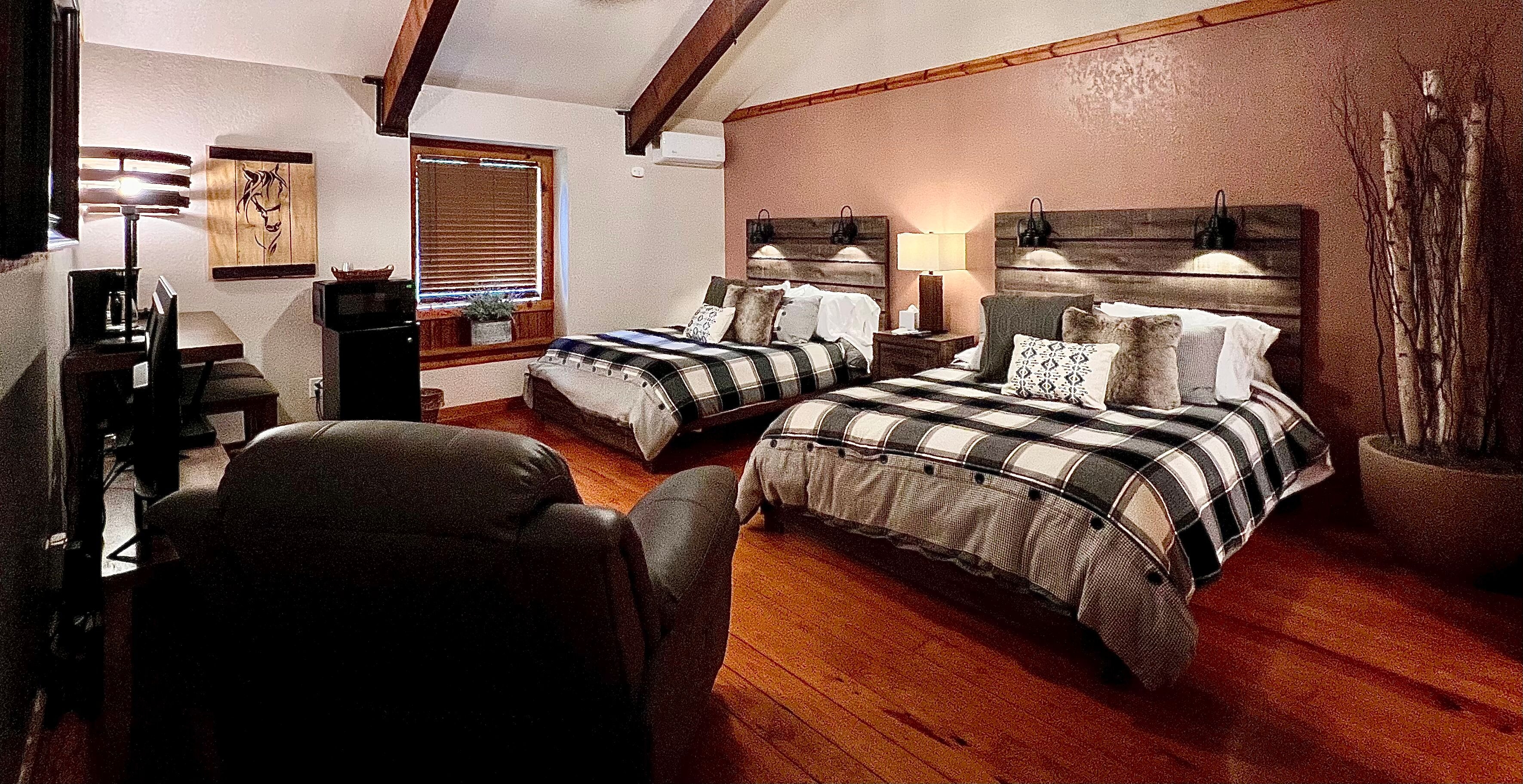 Spacious room with two queen beds side by side with lighted rustic headboards, leather recliner, and finished hardwood floor