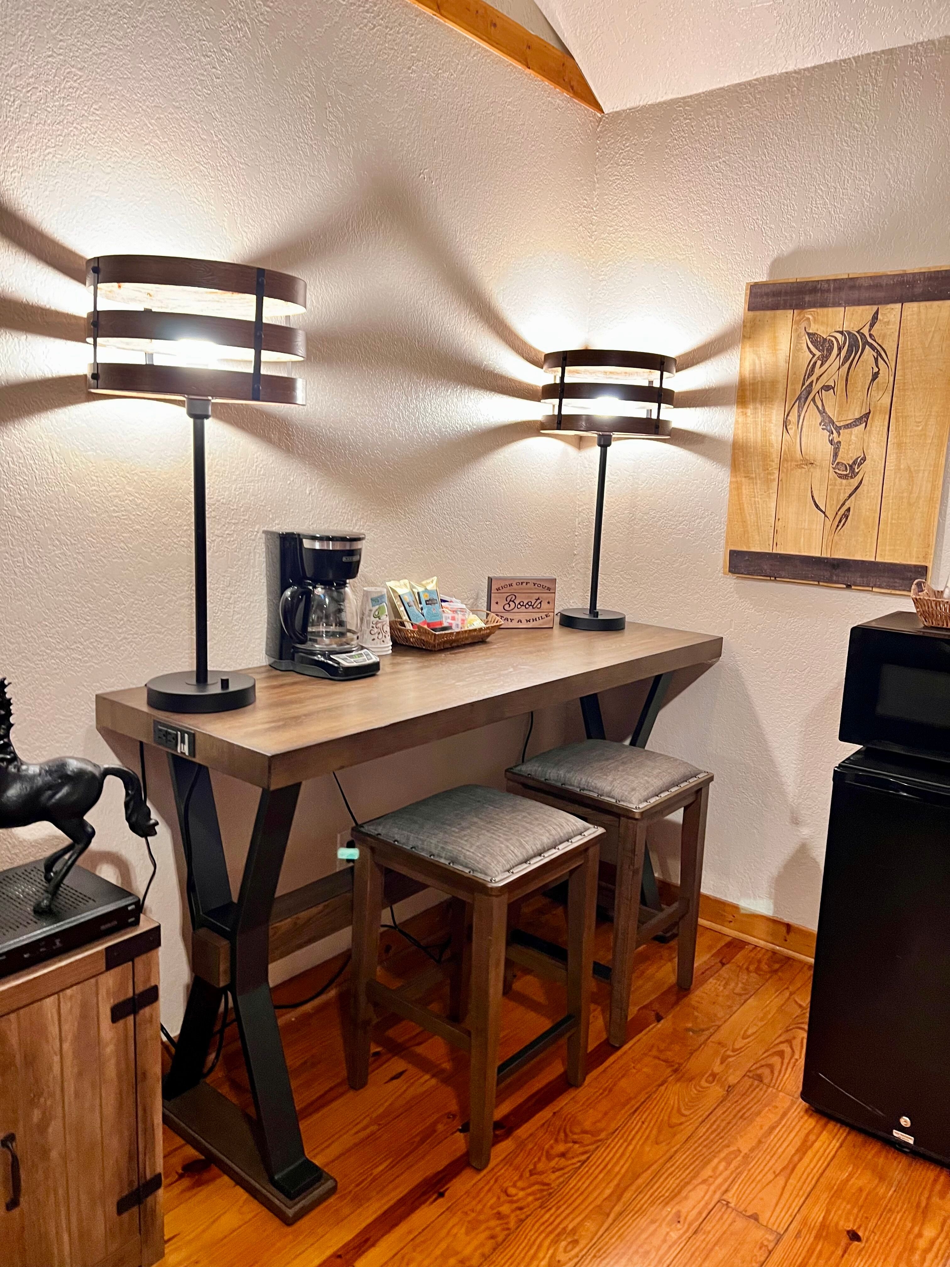 Coffee bar with two stools, coffee maker, mini-fridge, and microwave, horse-themed artwork on wall