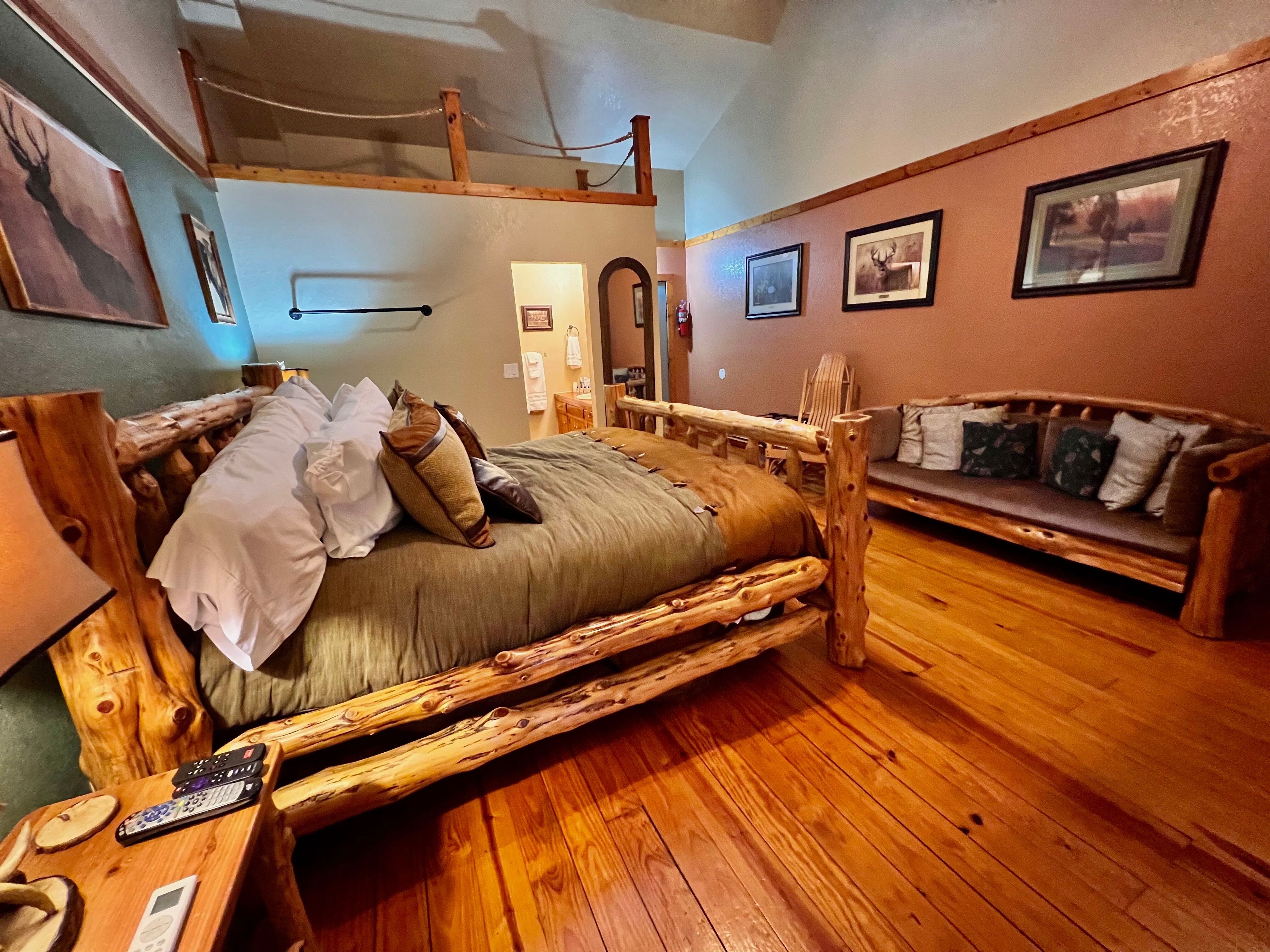 Spacious room with handcrafted log bed, matching couch with cushions against opposite wall, hardwood floors