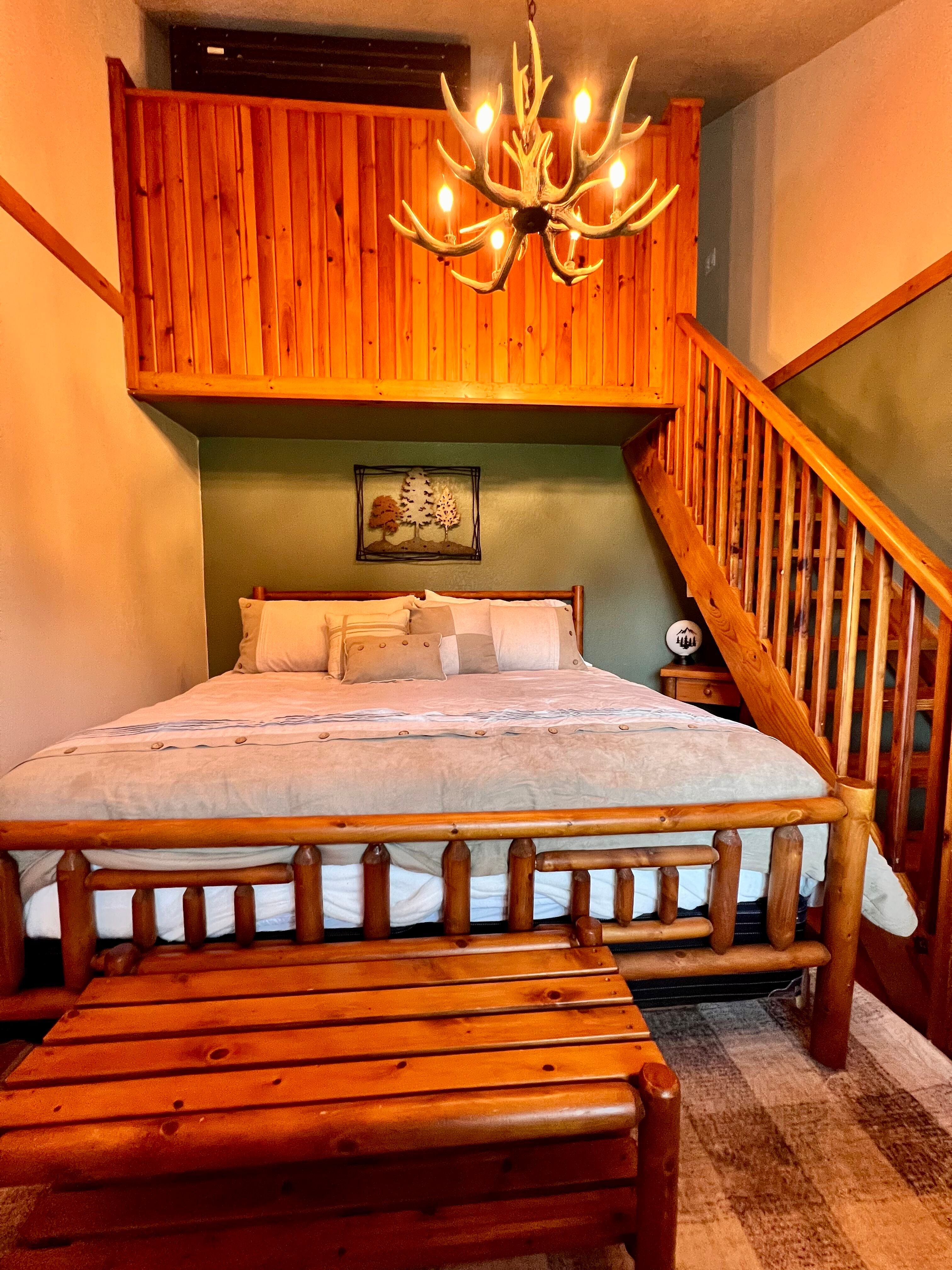 Handcrafted log bed with matching bench at foot, stairway leading to second floor, antler chandelier