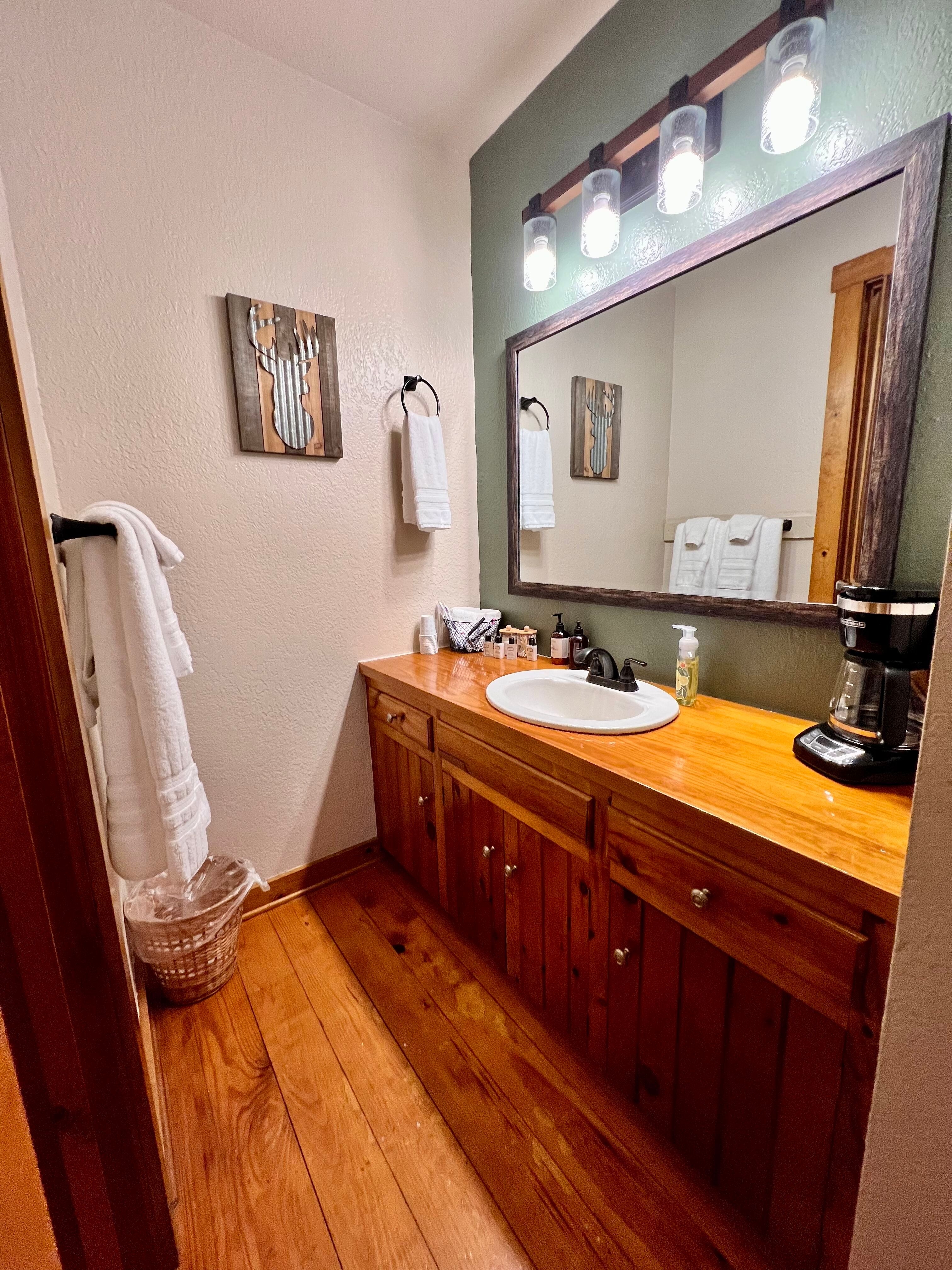 View of bathroom from doorway, beautifully stained wood vanity with white sink, mirror with lights above