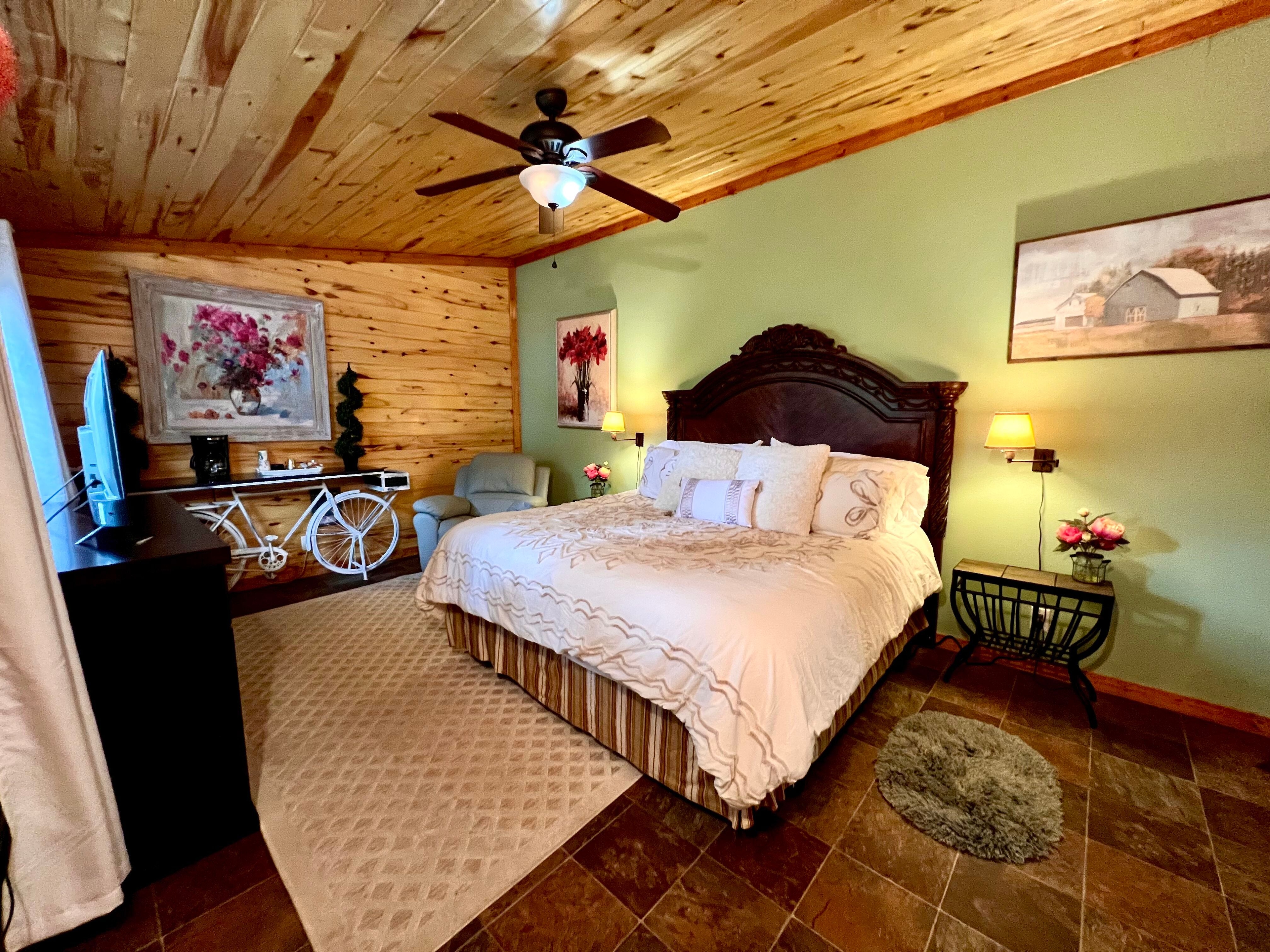 Romantic room with natural wood wall and ceilings, ceiling fan, king bed with elegant wooden headboard and sumptuous bedding, unique bicycle coffee bar