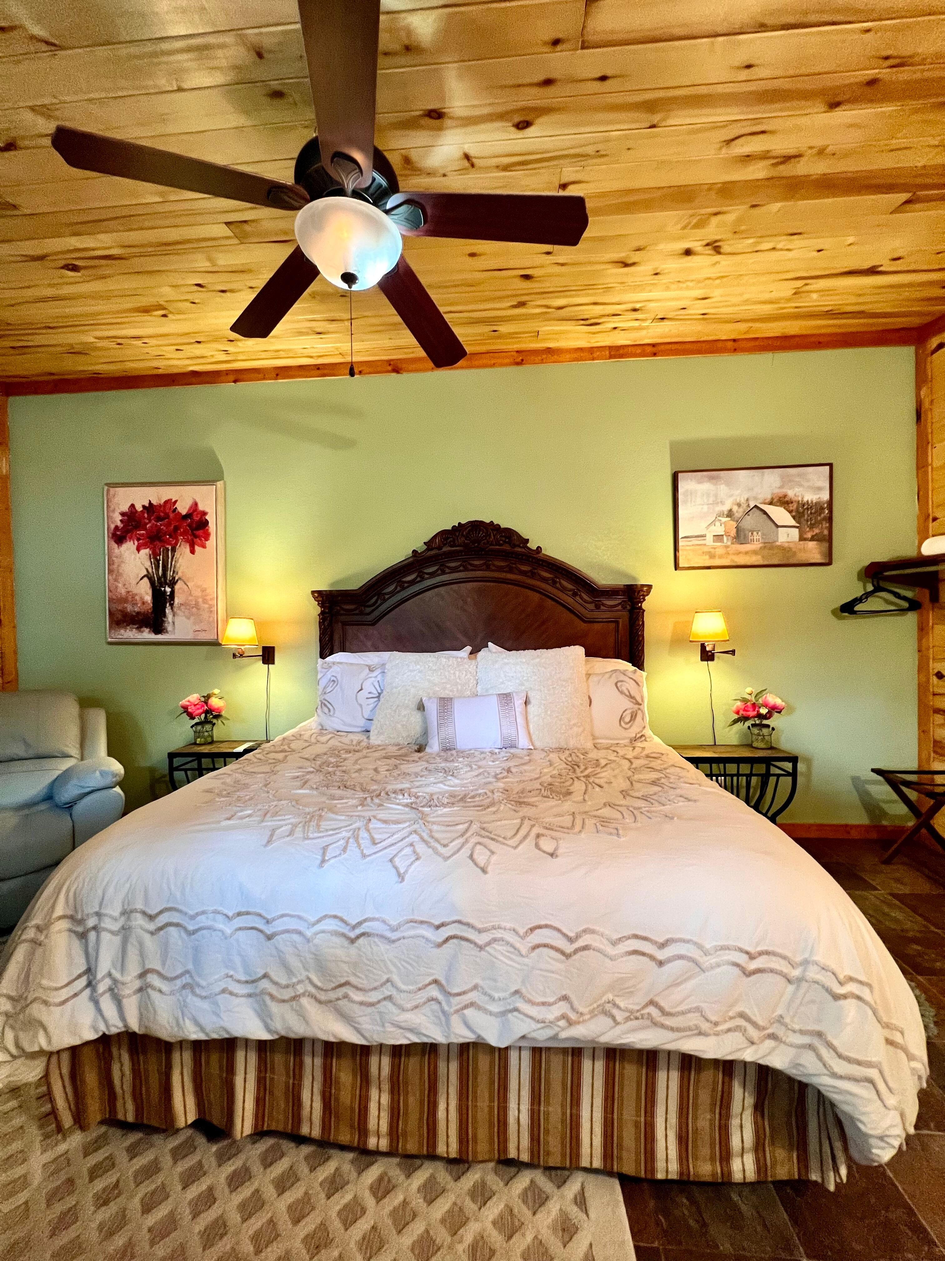 King bed with Victorian-style carved wood headboard, lofty bedding, natural wood ceiling and ceiling fan