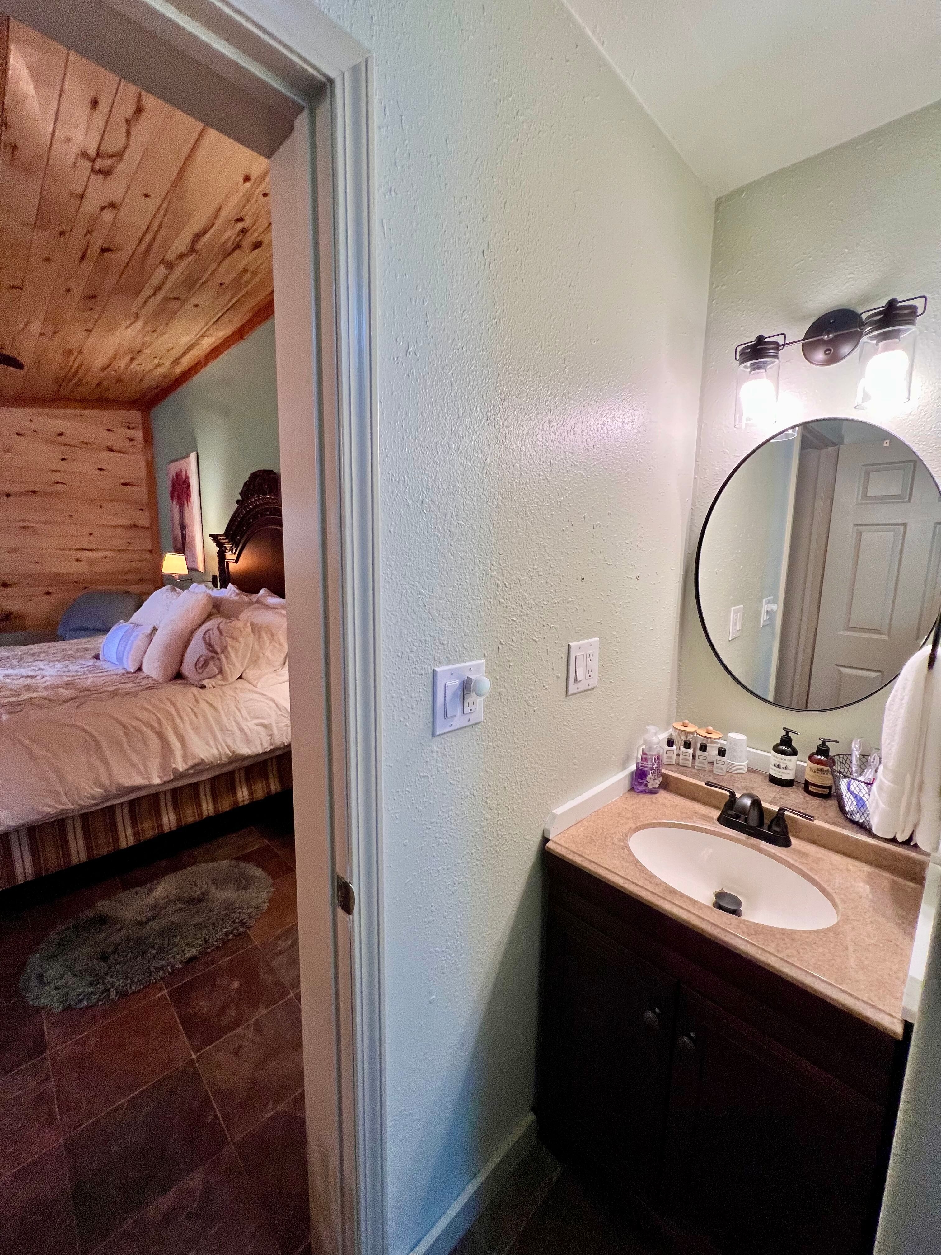 Bathroom vanity with mirror and lights overhead, doorway leading into bedroom