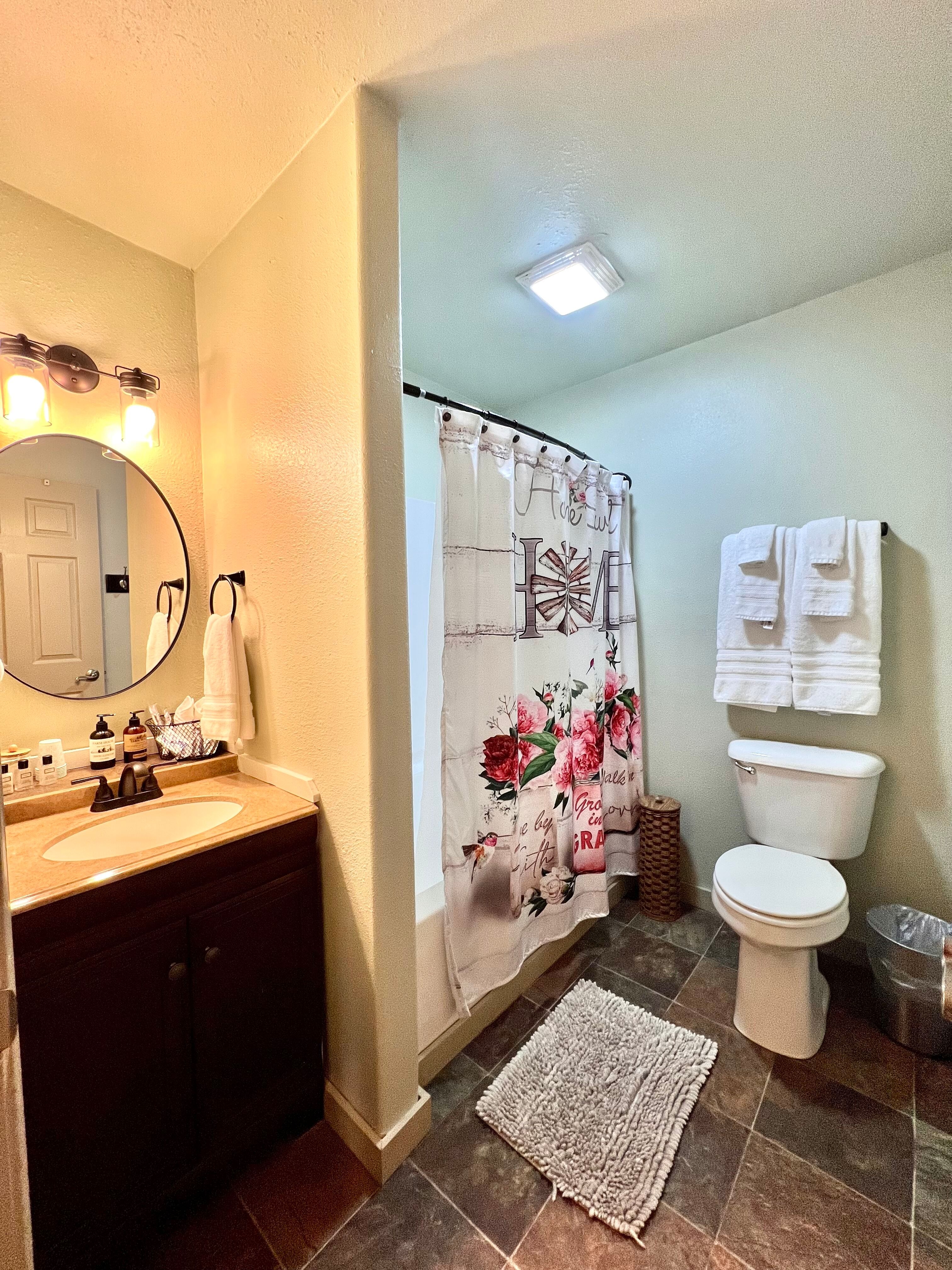 Bathroom with vanity & sink, shower with floral curtain, toilet, and plush white towels hanging on rack