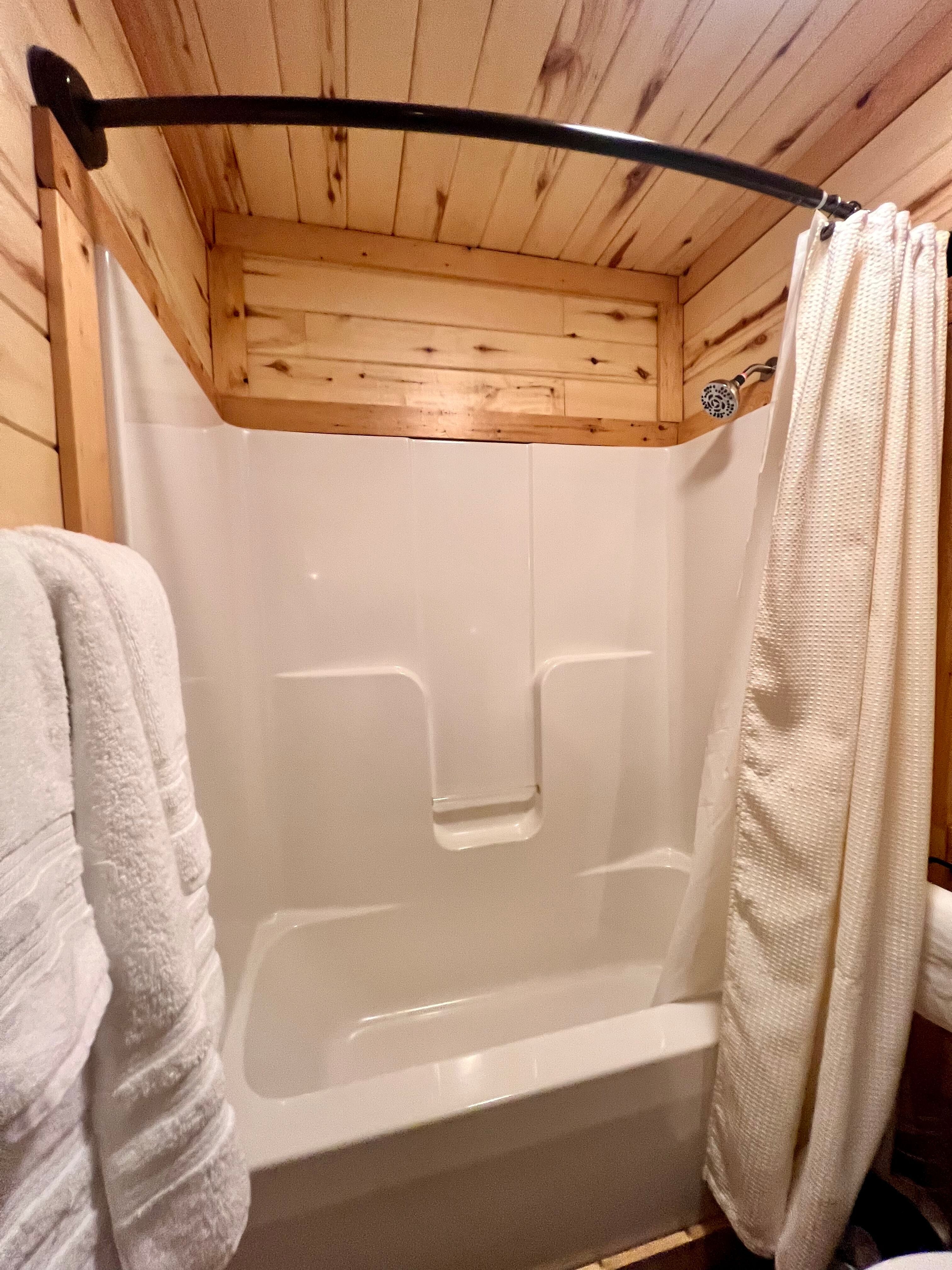 Gleaming white shower with plush white towels hanging on natural pine wood walls