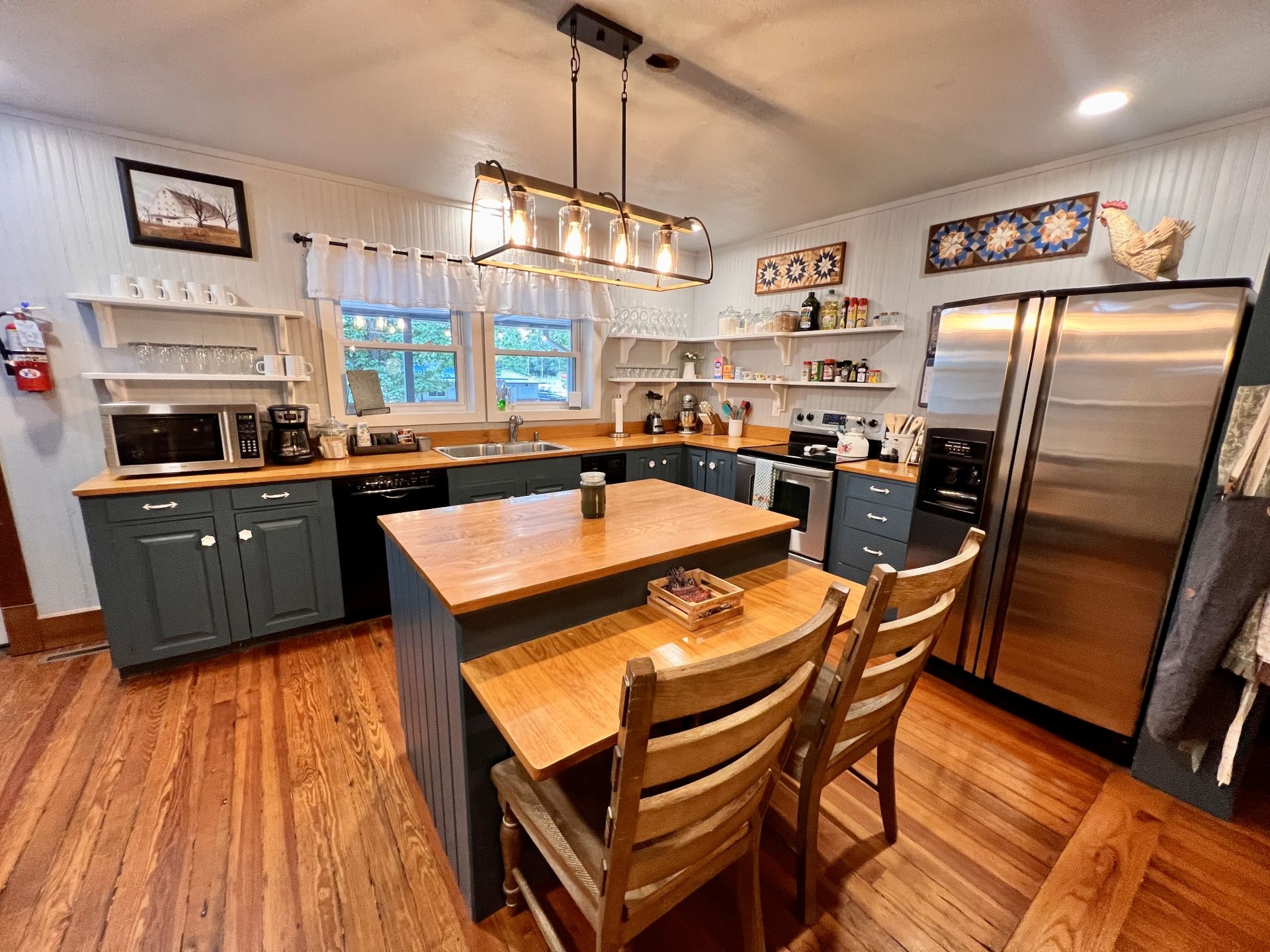 Brightly lit kitchen with painted cabinets, dishwasher, stove, stainless refrigerator, and kitchen island with chairs and breakfast bar