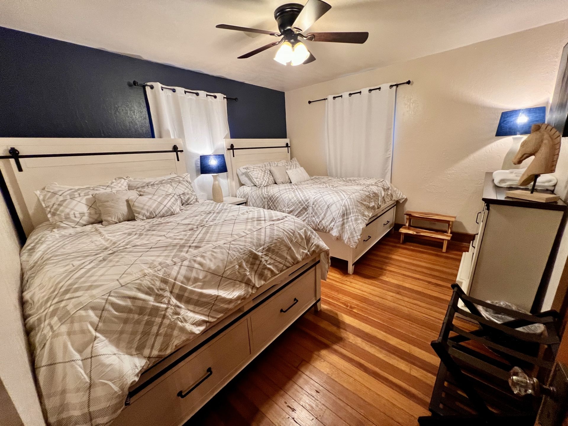 Cozy bedroom with two beds, blue and white paint scheme, ceiling fan, and beautifully finished wood floors